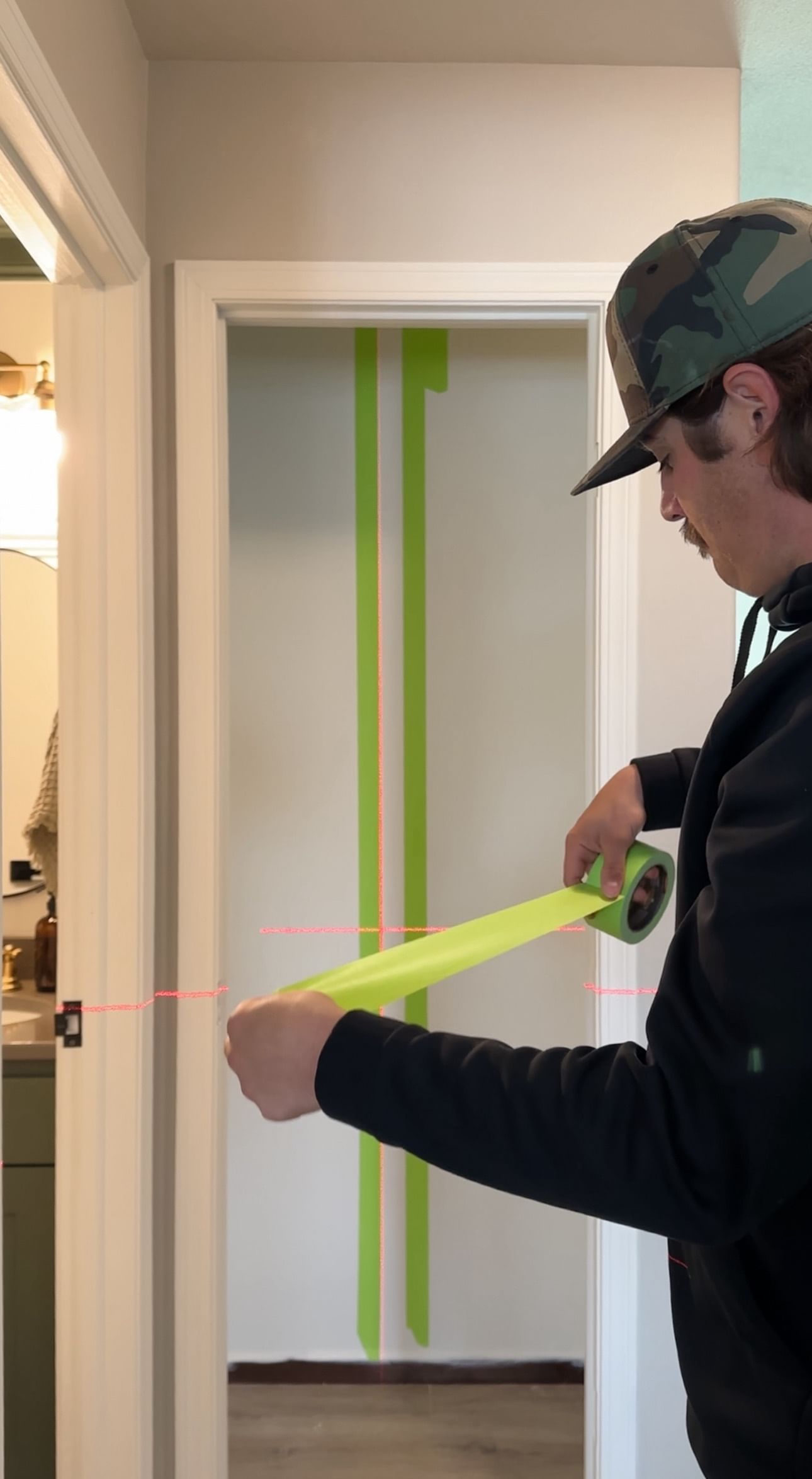 A man using a laser level to apply vertical strips of FrogTape Advanced straight.