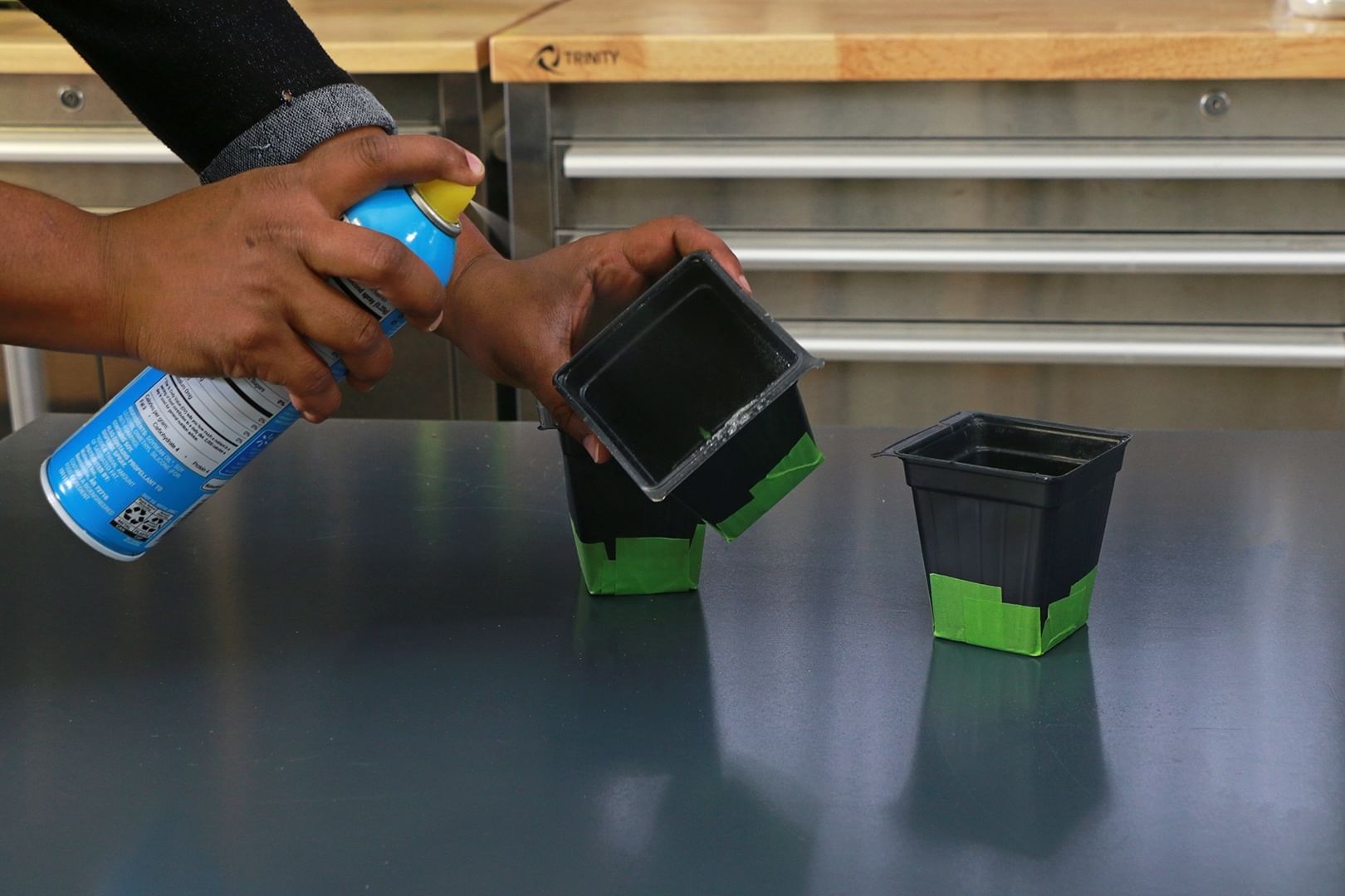 Close up shot of hands spray painting 3 small black planters with tape placed