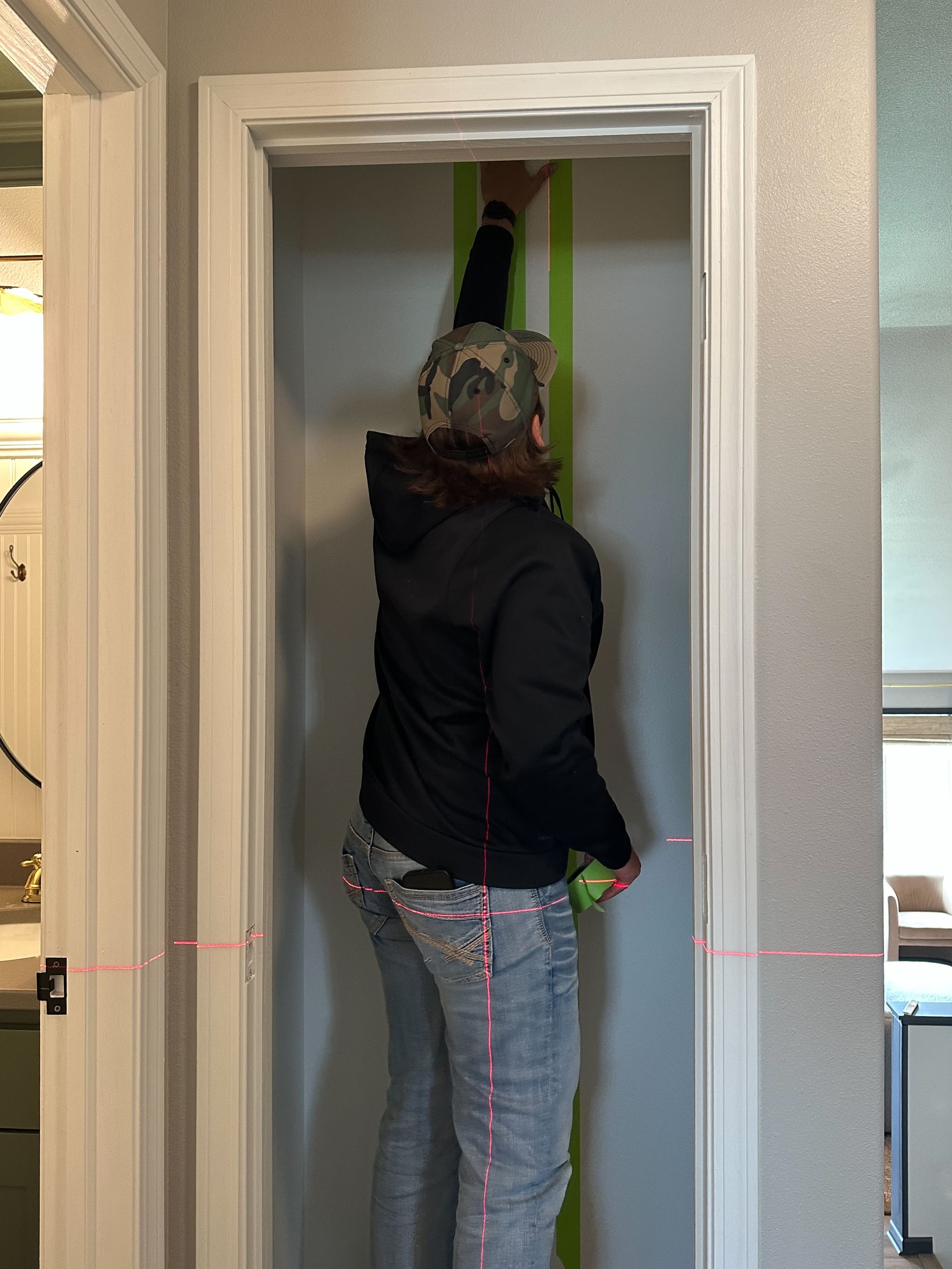 A man using a laser level to apply vertical strips of FrogTape Advanced straight.