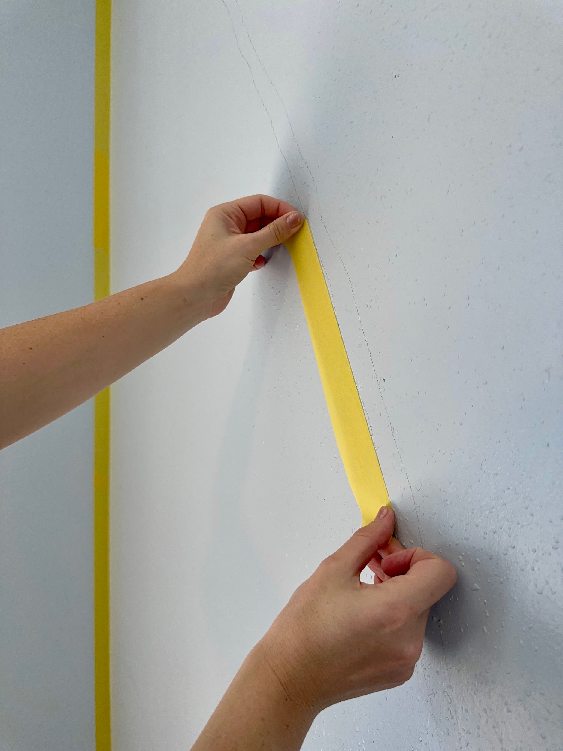 Yellow FrogTape Delicate Surface Painter's Tape being placed on a blue wall, covering a penciled sketched line