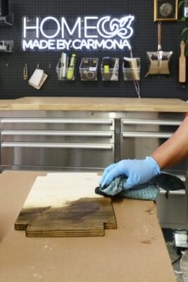 Hand rubbing stain on a wooden tray with a cloth/rag.