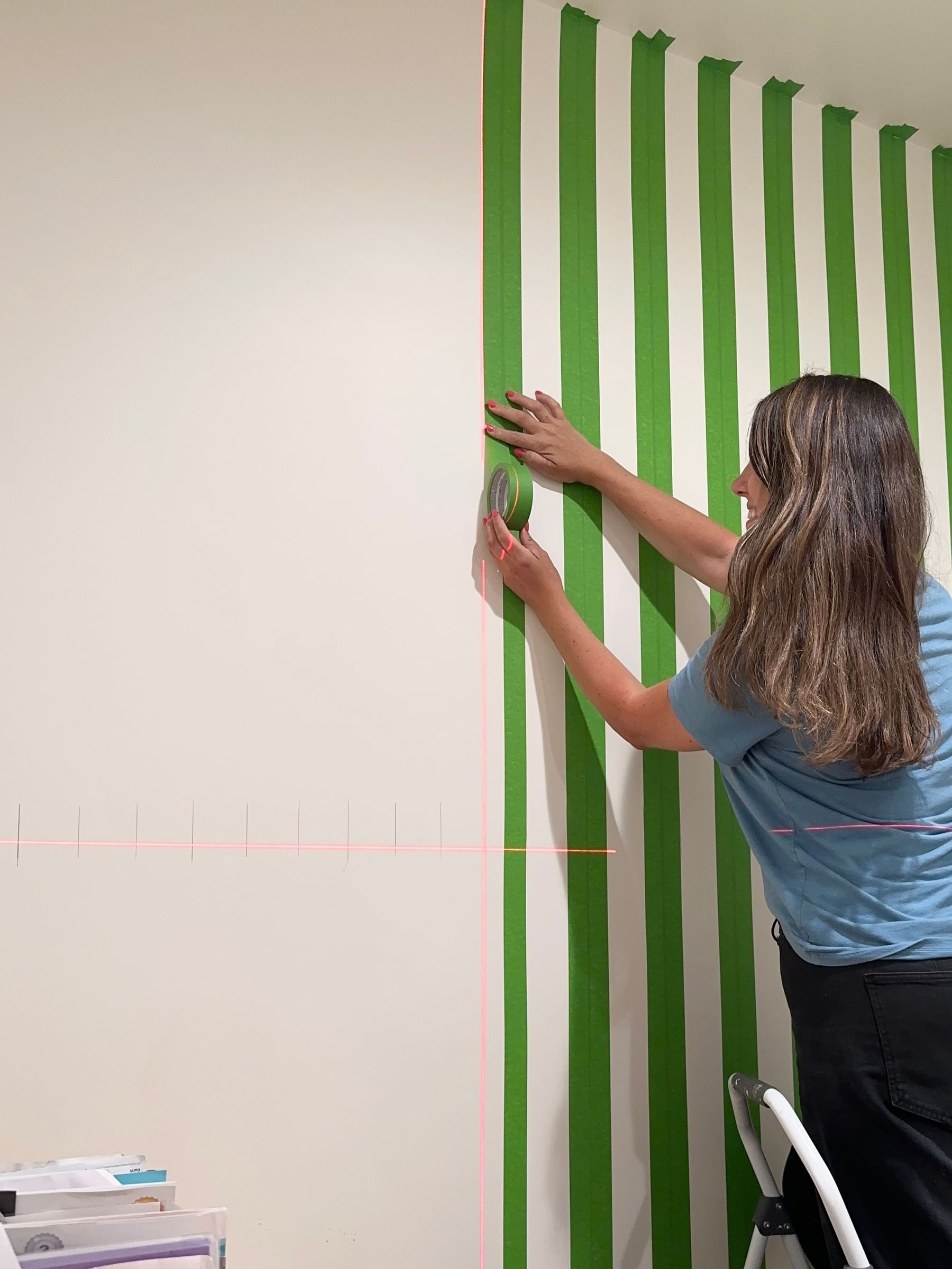 Haylee Griffin Taping vertical stripes of Green FrogTape Multi-Surface Painters Tape to a white wall