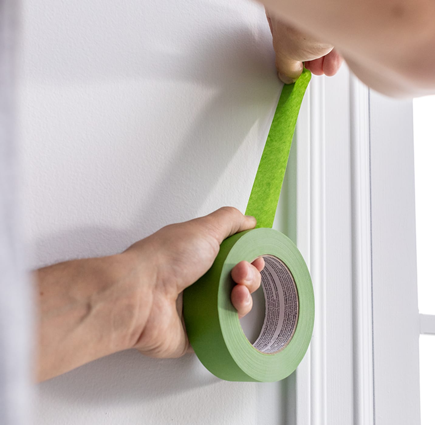 Painter pulling green multi-surface tape up to place on corner trim