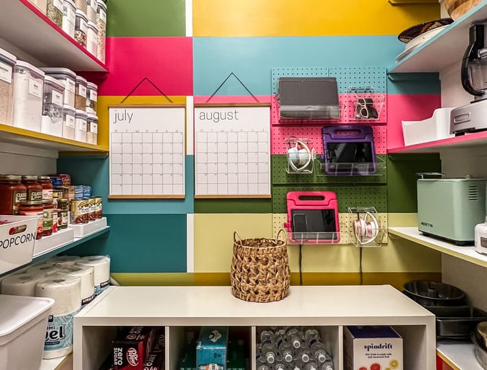 Colorful pantry with organized shelves and storage. Wall calendars for July and August are centered among bright squares. Neat, tidy, and vibrant setting.