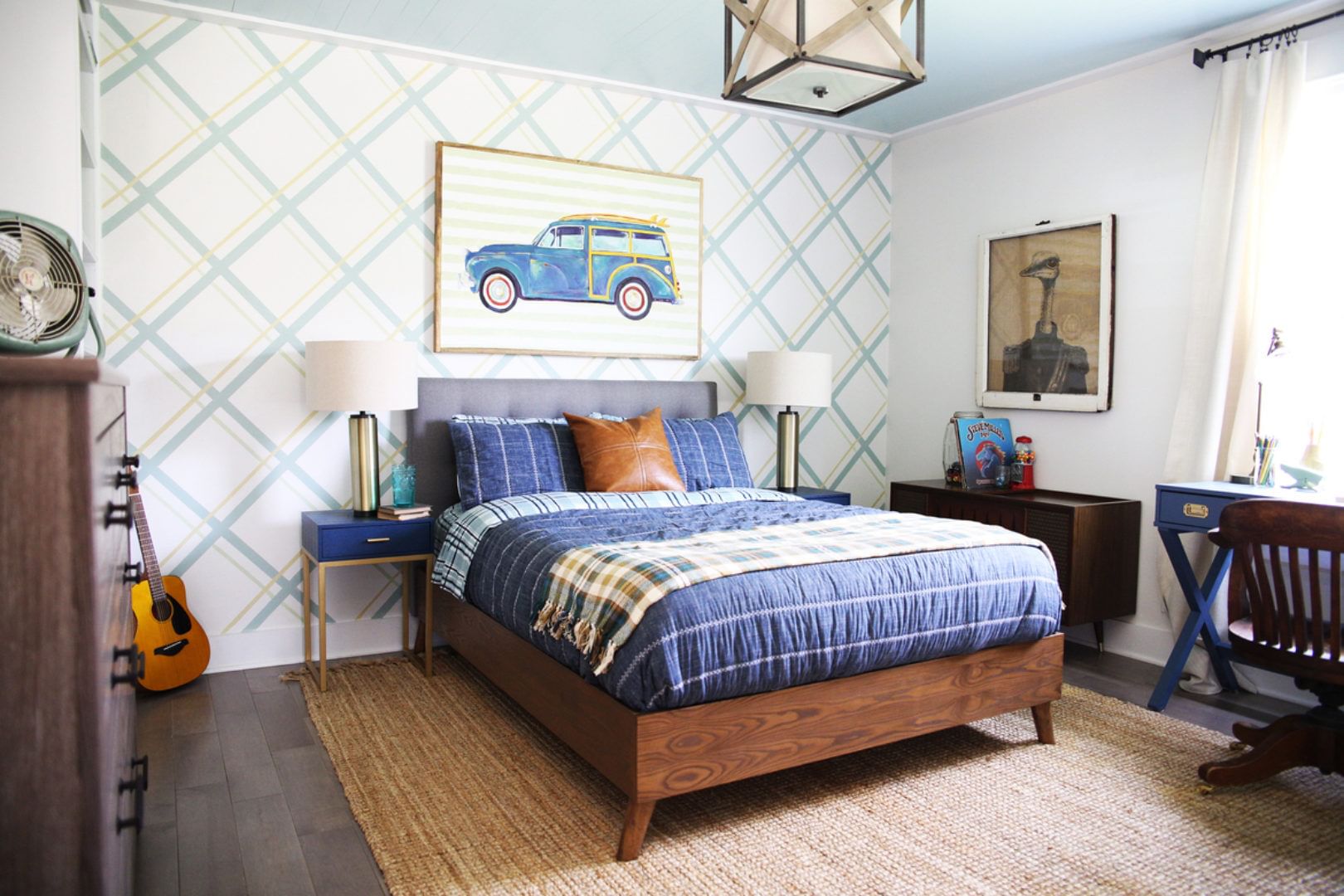 Bedroom with brown dresser, desk and bed. The back wall has diagonal gray lines running across and there is a picture of a car above the bed