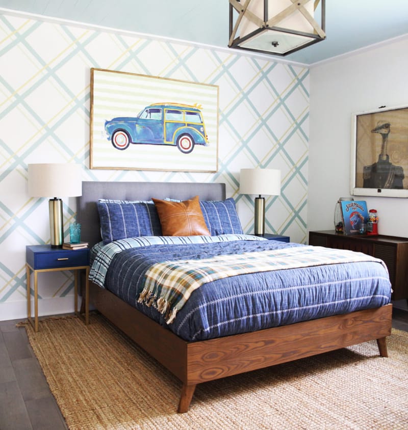 Bedroom with brown dresser, desk and bed. The back wall has diagonal gray lines running across and there is a picture of a car above the bed