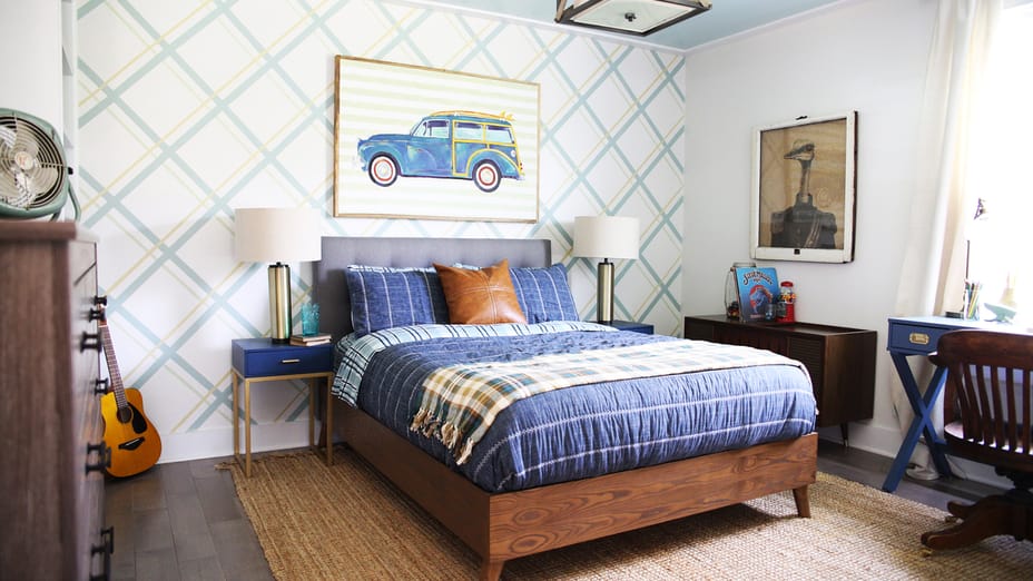 Bedroom with brown dresser, desk and bed. The back wall has diagonal gray lines running across and there is a picture of a car above the bed