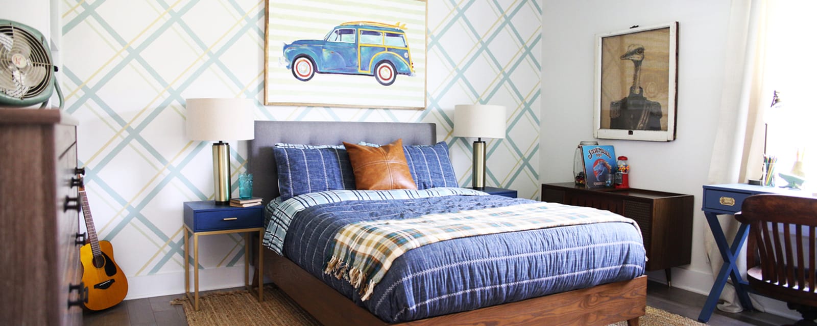 Bedroom with brown dresser, desk and bed. The back wall has diagonal gray lines running across and there is a picture of a car above the bed