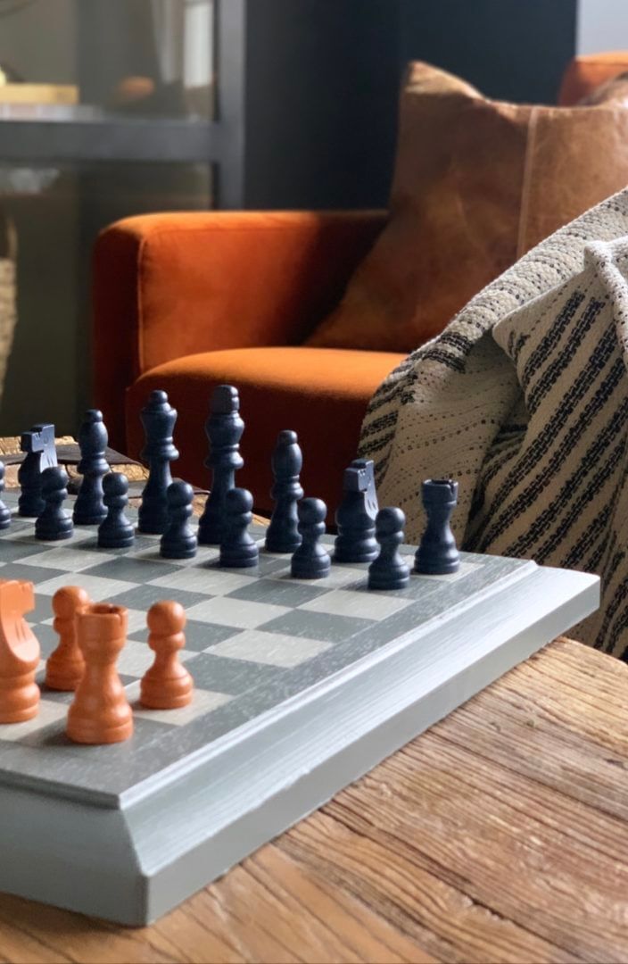 Grey chess board with white and grey checkered pattern on a wooden table. There are brown and black pieces lines on the chess board