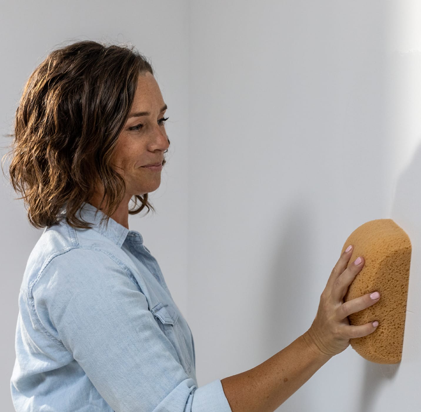 Una mujer limpiando una pared blanca con una esponja