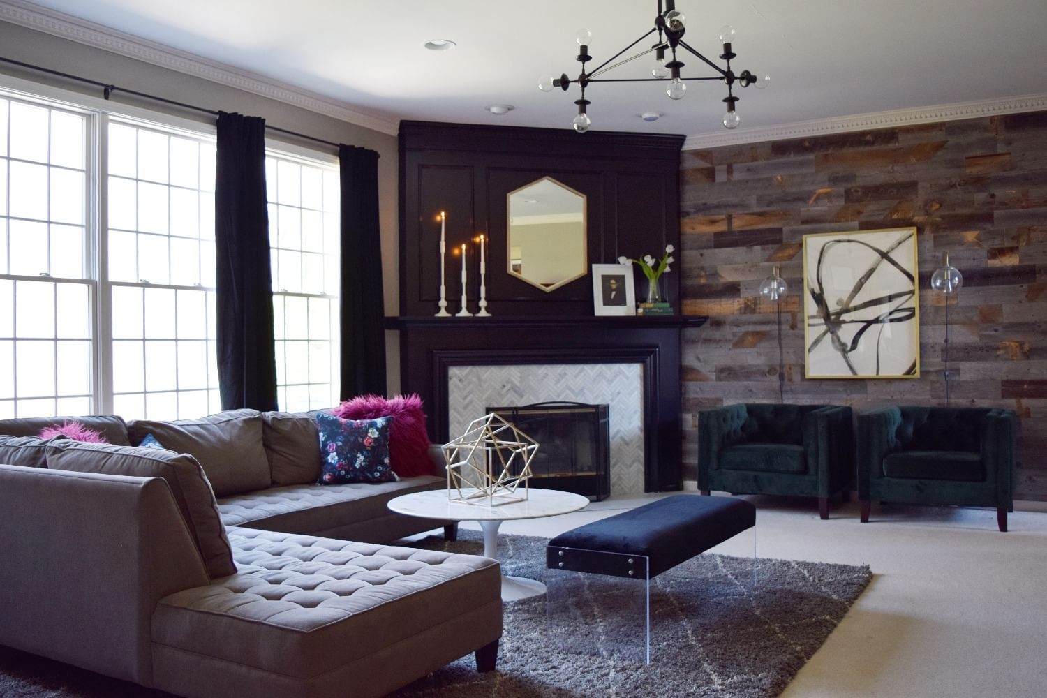 Modern living room with tufted brown sectional, geometric decor on marble coffee table, and dark wood fireplace. Art and candles add elegance.