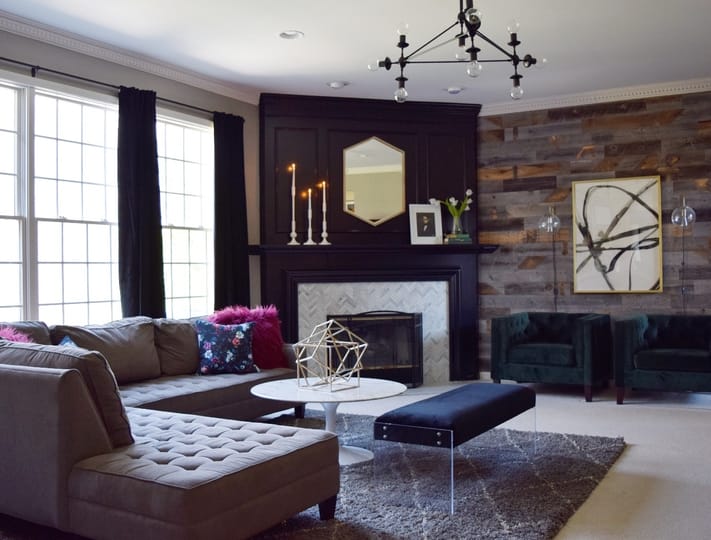 Modern living room with tufted brown sectional, geometric decor on marble coffee table, and dark wood fireplace. Art and candles add elegance.