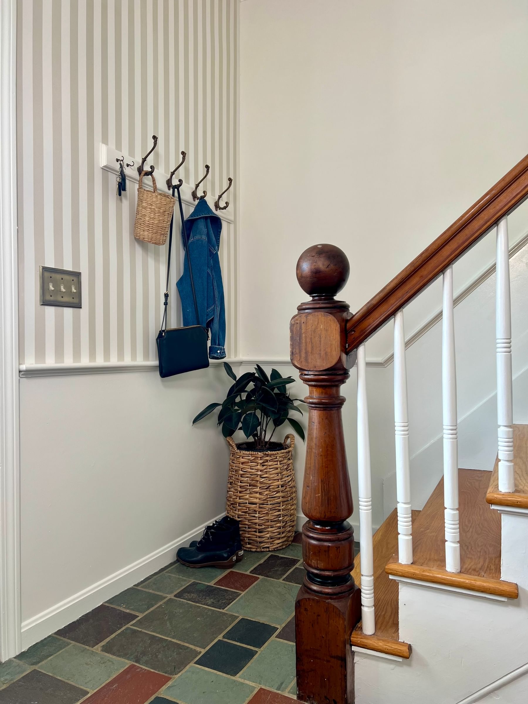 Foyer area with staircase railing. The walls are striped with wainscotting at the bottom