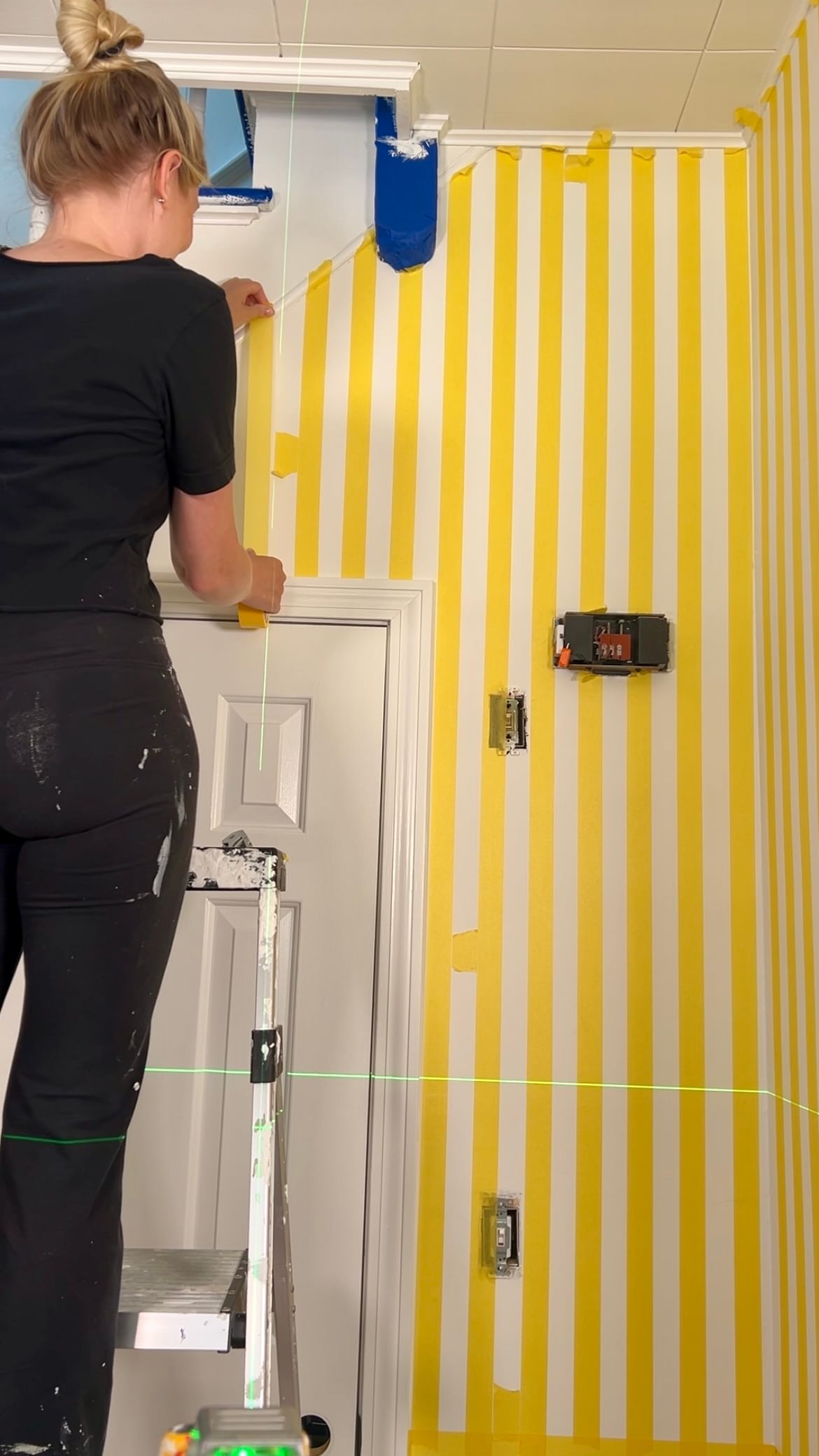 Haley Poole Taping vertical stripes on a wall with yellow FrogTape Delicate Surface Painters Tape