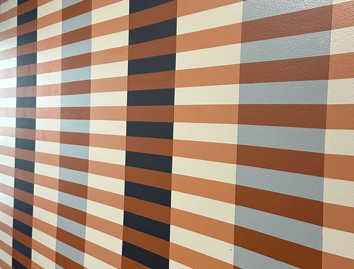 Striped pattern wall with vertical brown, cream, and dark blue bands intersected by horizontal lines, creating a retro, geometric aesthetic.