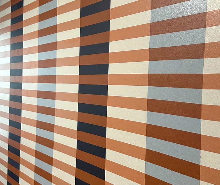 Striped pattern wall with vertical brown, cream, and dark blue bands intersected by horizontal lines, creating a retro, geometric aesthetic.