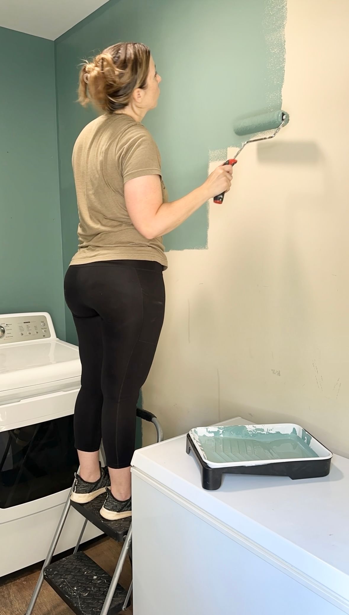 Katie Sharp painting a laundry room wall blue with a paint roller