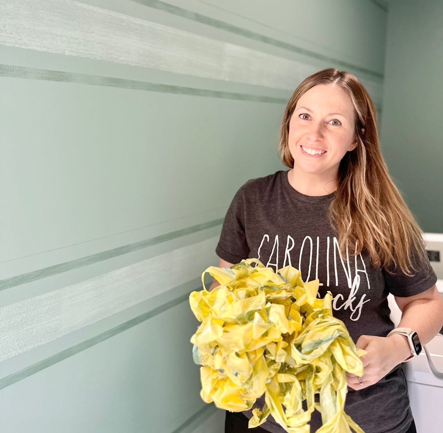 Katie Sharpe holding a bundle of the used Yellow Delicate Surface Painter's Tape. There are crisp horizontal paint lines on the wall behind her.