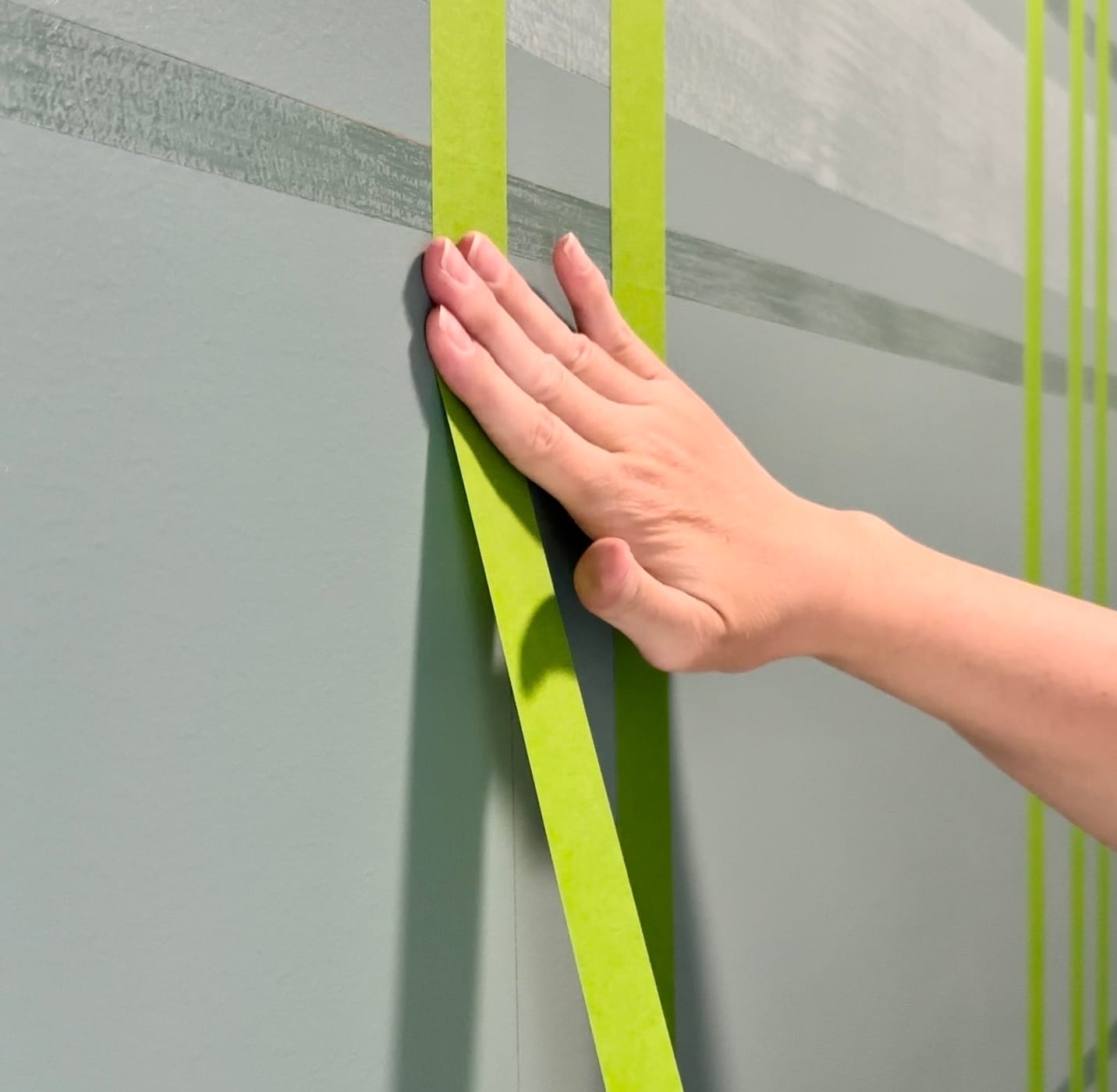 A hand taping a vertical line of Green FrogTape Multi-Surface Painter's Tape