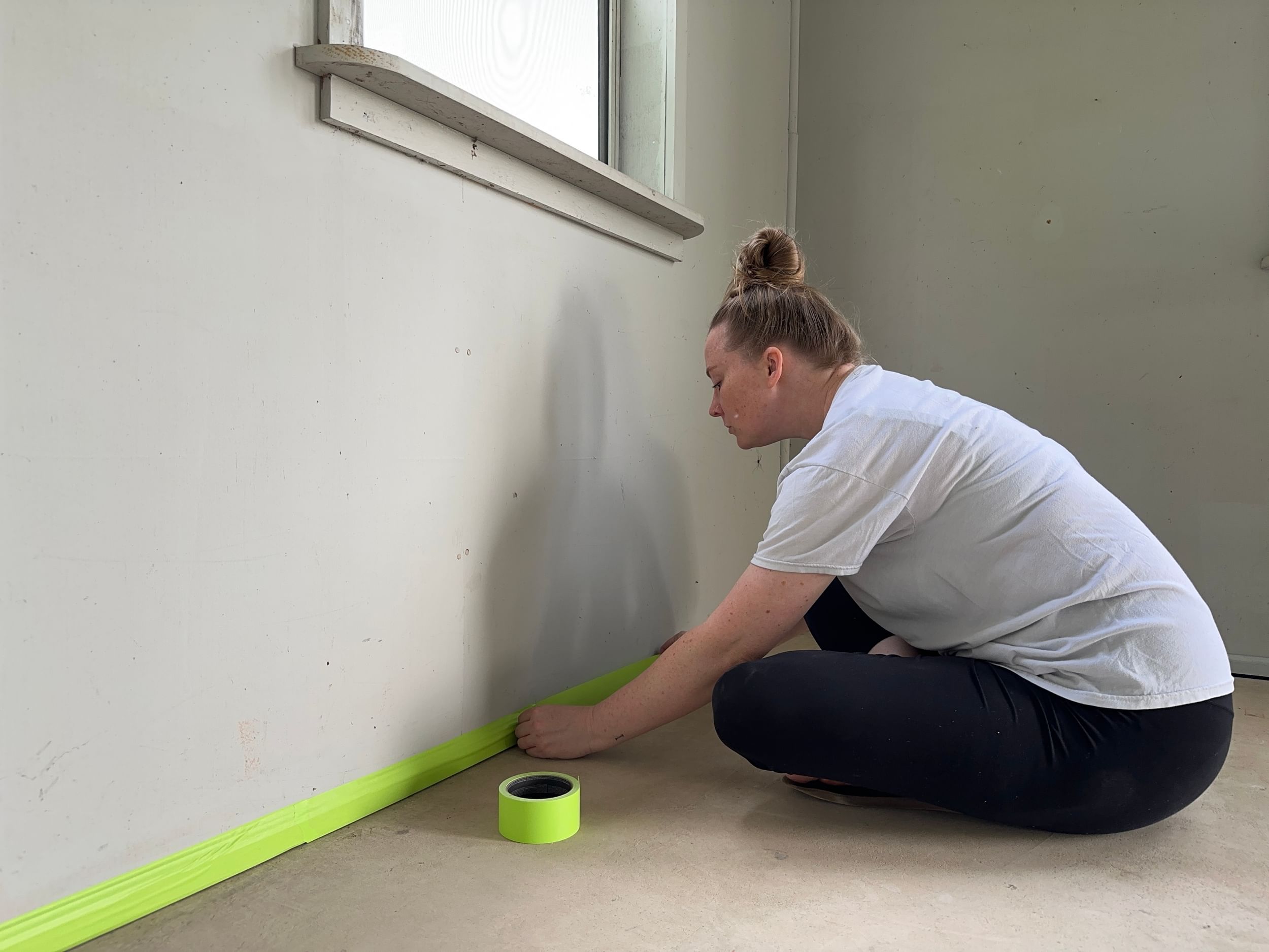 Woman taping off where the wall meets the floor with FrogTape Advanced